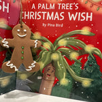 Close-up of A Palm Tree’s Christmas Wish children’s book by Pina Bird with a smiling gingerbread man ornament, festive red holiday background, and illustrated palm tree character.