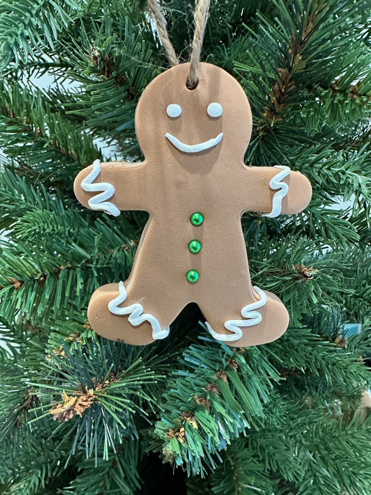 Smiling gingerbread man ornament hanging on a green Christmas tree, festive holiday decoration featured in Pina Bird’s A Palm Tree’s Christmas Wish.