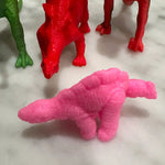 Colorful toy dinosaurs, with a pink dinosaur in the foreground, surrounded by red and green ones.